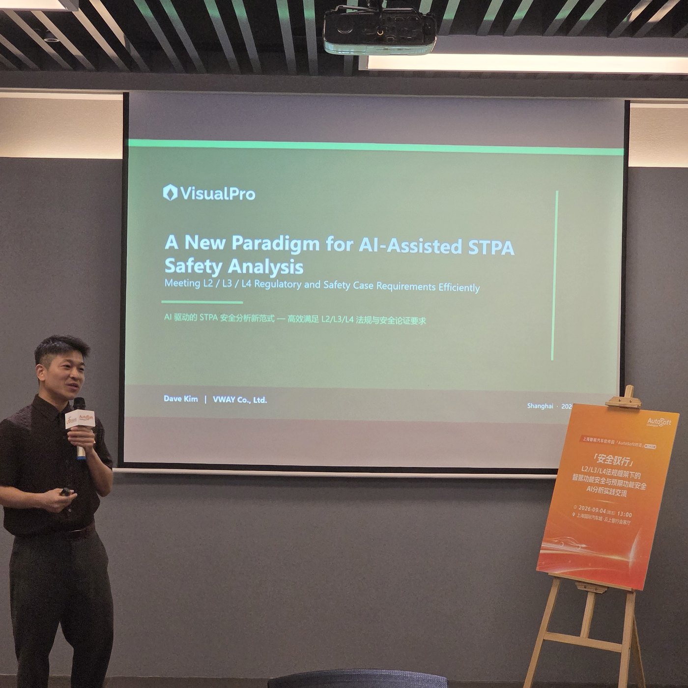 VWAY 演讲者手持话筒，身后是开场幻灯片「A New Paradigm for AI-Assisted STPA Safety Analysis」